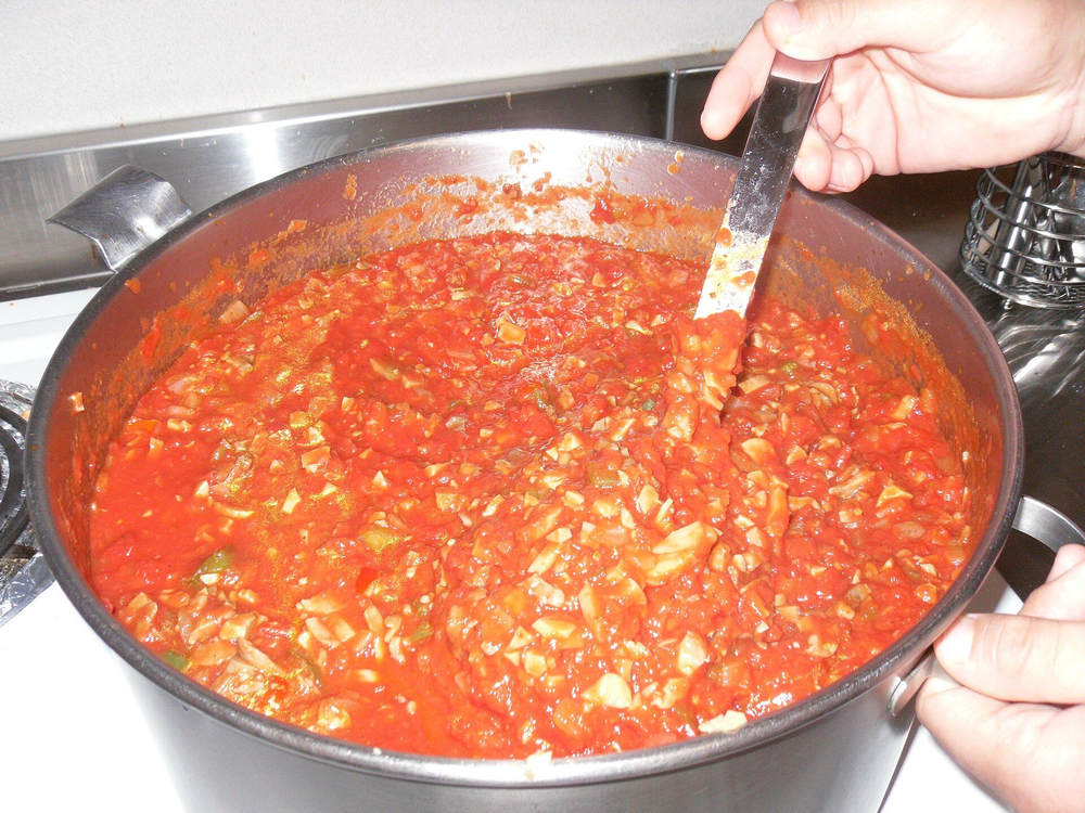 Een grote kookpan met pastasaus die wordt omgeroerd
